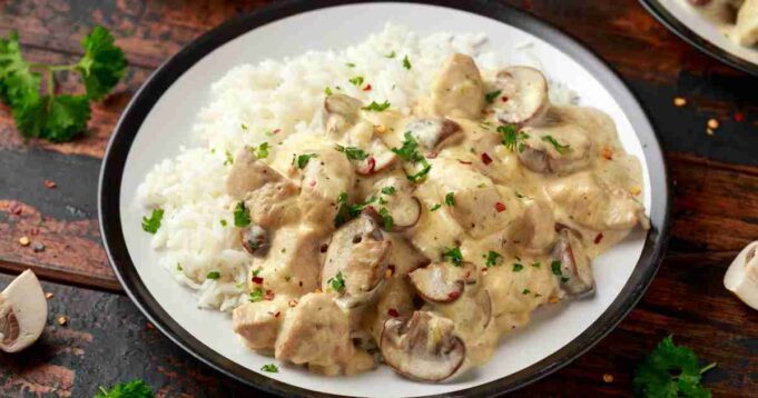 A skillet filled with creamy chicken and mushrooms garnished with fresh herbs.