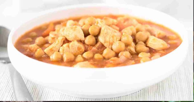 A hearty bowl of Cumin Chicken & Chickpea Stew garnished with fresh herbs and a slice of crusty bread.