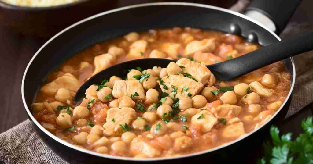 A hearty bowl of Cumin Chicken & Chickpea Stew garnished with fresh herbs and a slice of crusty bread. cumin chicken &amp;amp; chickpea stew Cumin Chicken &#038; Chickpea Stew Cumin Chicken Chickpea Stew1 1024x538