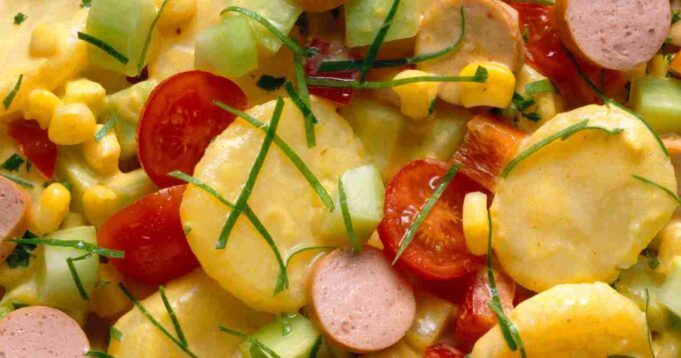 A vibrant bowl of Curried Potato Salad garnished with fresh herbs and spices.