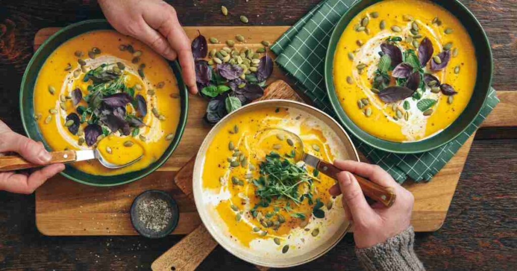A creamy bowl of homemade pumpkin soup garnished with pumpkin seeds and a sprig of fresh thyme. pumpkin soup Classic Velvety Pumpkin Soup Easy pumpkin soup recipe 1024x538