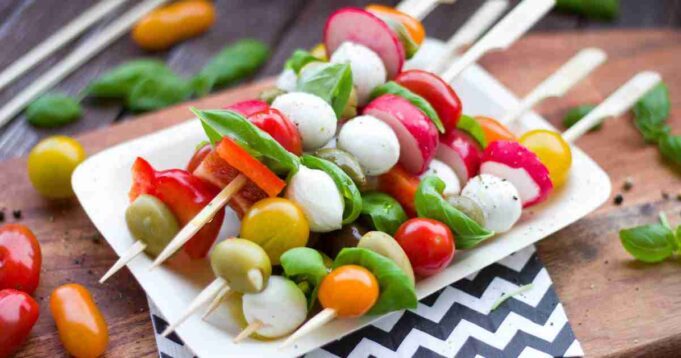 Colorful Greek Salad Skewers neatly arranged on a white platter with a side of tzatziki sauce.
