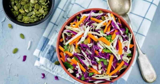 A vibrant bowl of Spicy Cabbage Slaw, bursting with colours of red and green cabbage, carrots, and a tangy dressing.