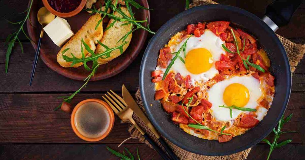 Aromatic Spicy Moroccan Eggs simmering in a cast iron skillet with vibrant tomatoes and herbs. spicy moroccan eggs Spicy Moroccan Eggs Spicy Moroccan eggs 1024x538