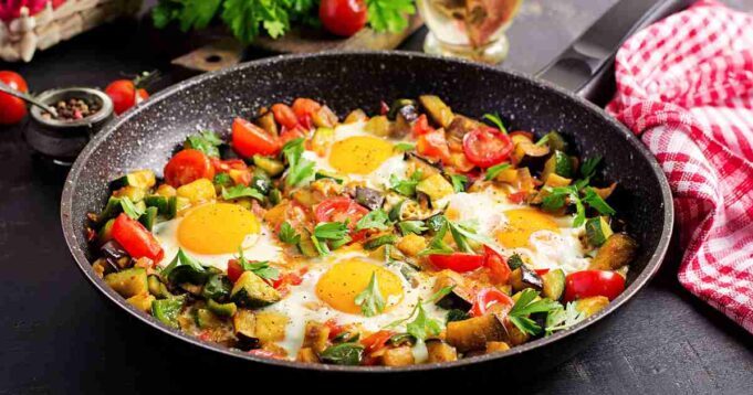 Aromatic Spicy Moroccan Eggs simmering in a cast iron skillet with vibrant tomatoes and herbs.