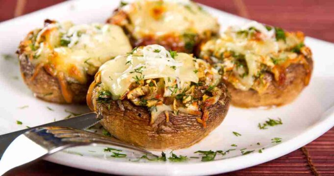Golden-browned stuffed mushrooms filled with a savory mixture of herbs, cheese, and breadcrumbs on a white serving platter.