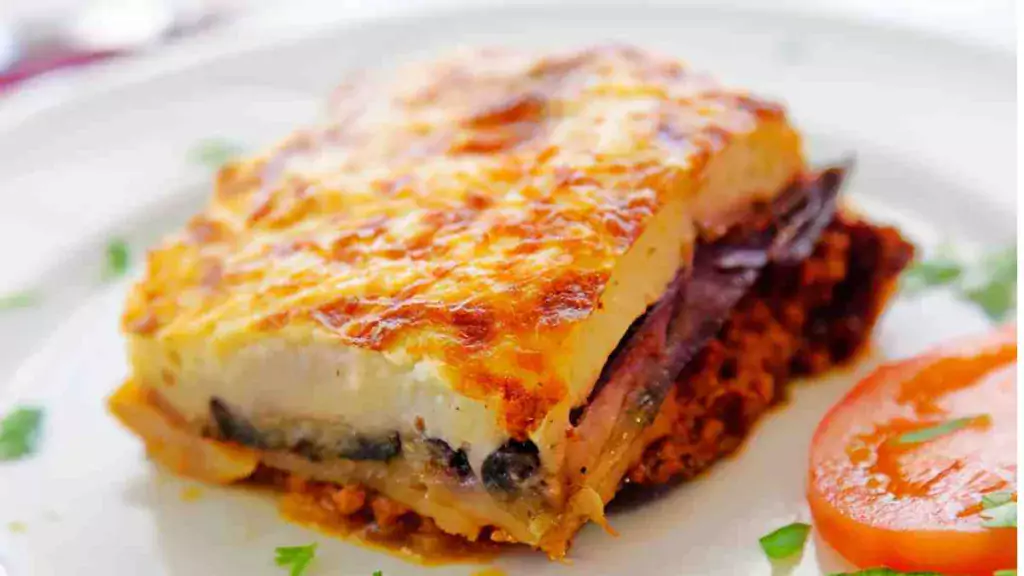 A healthy and delicious serving of low-fat moussaka with layers of eggplant, meat sauce, and creamy topping on a white plate. low-fat moussaka Low-Fat Moussaka Recipe Low Fat Moussaka 1024x576