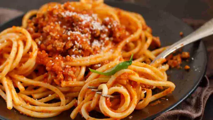 Hearty and savory big-batch bolognese sauce over pasta in a white bowl.